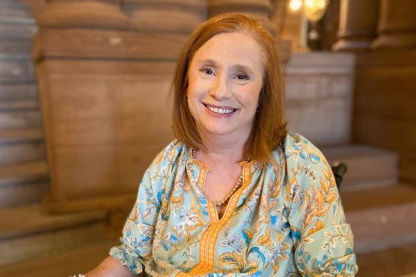 Kimberly Hill, 红头发，蓝黄色衬衫, 坐在轮椅上，坐在奥尔巴尼的国会大厦里, smiling.